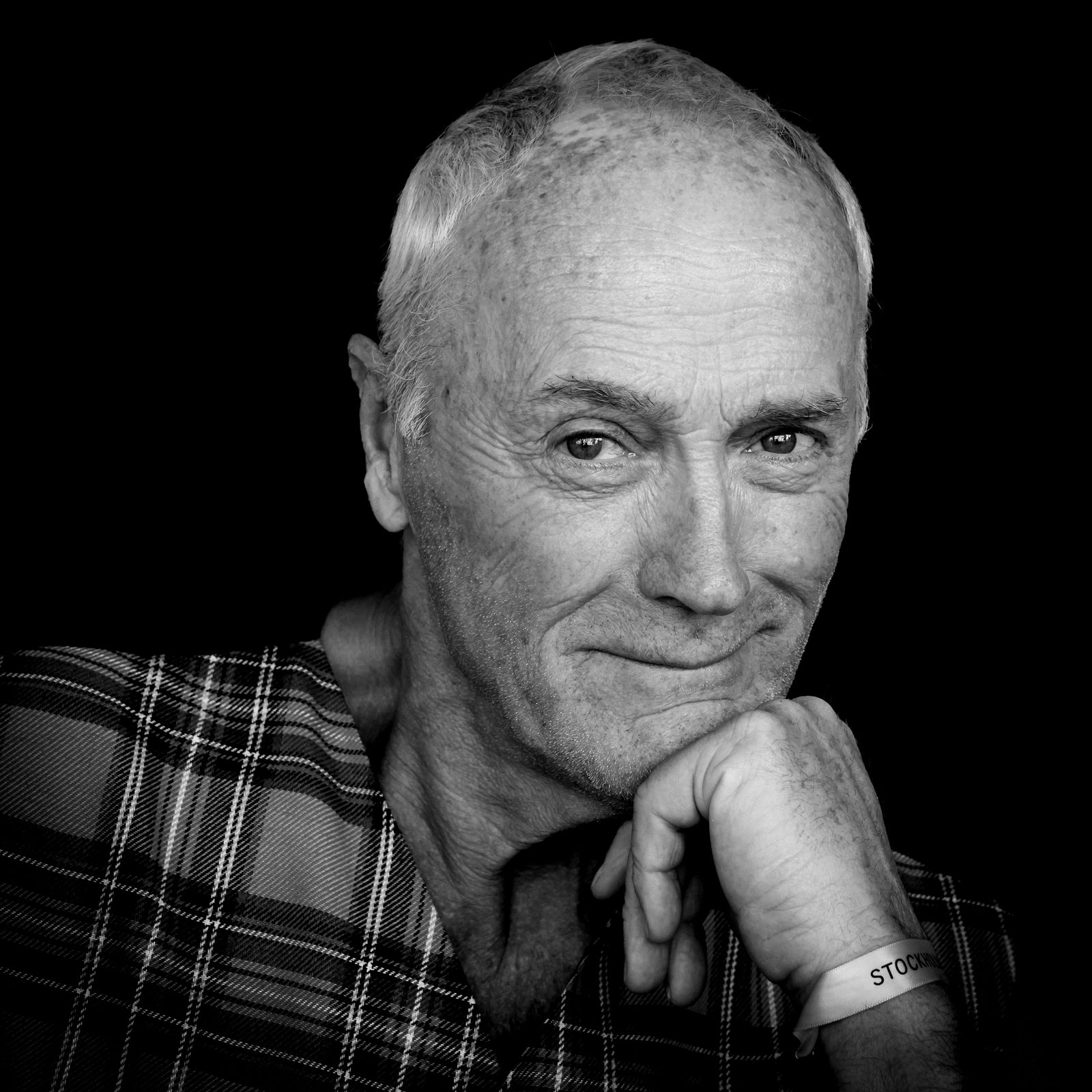 Olof Näslund Black-and-white portrait of an older man in a plaid shirt, resting his chin on his hand and looking calmly into the camera.